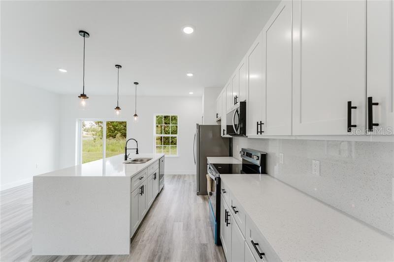 A modern kitchen features white cabinets, quartz countertops, a center island, and stainless steel appliances — 16204 SW 27TH TERRACE ROAD, OCALA, FL