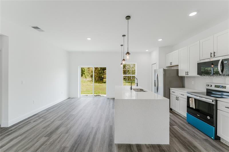 A modern kitchen with white cabinets, a quartz island, and gray wood-look flooring — 16204 SW 27TH TERRACE ROAD, OCALA, FL