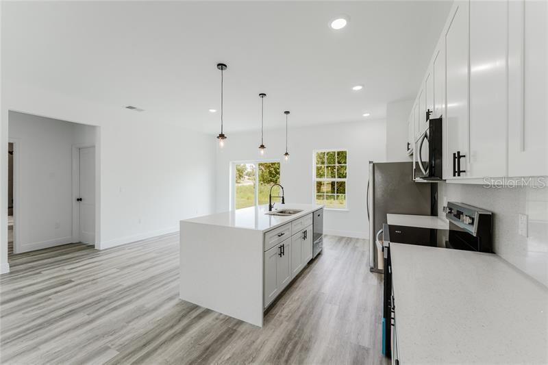 A modern kitchen features white cabinets, a central island with a sink, and light flooring — 16204 SW 27TH TERRACE ROAD, OCALA, FL
