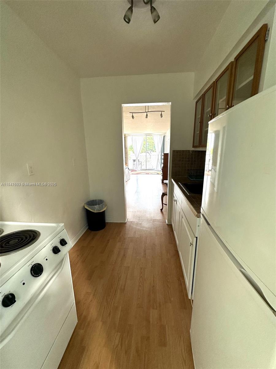 A galley kitchen features white appliances, wood-look flooring, and a doorway leading to a balcony — 1400 Pennsylvania Ave # 33, Miami Beach FL 33139, MIAMI BEACH, FL
