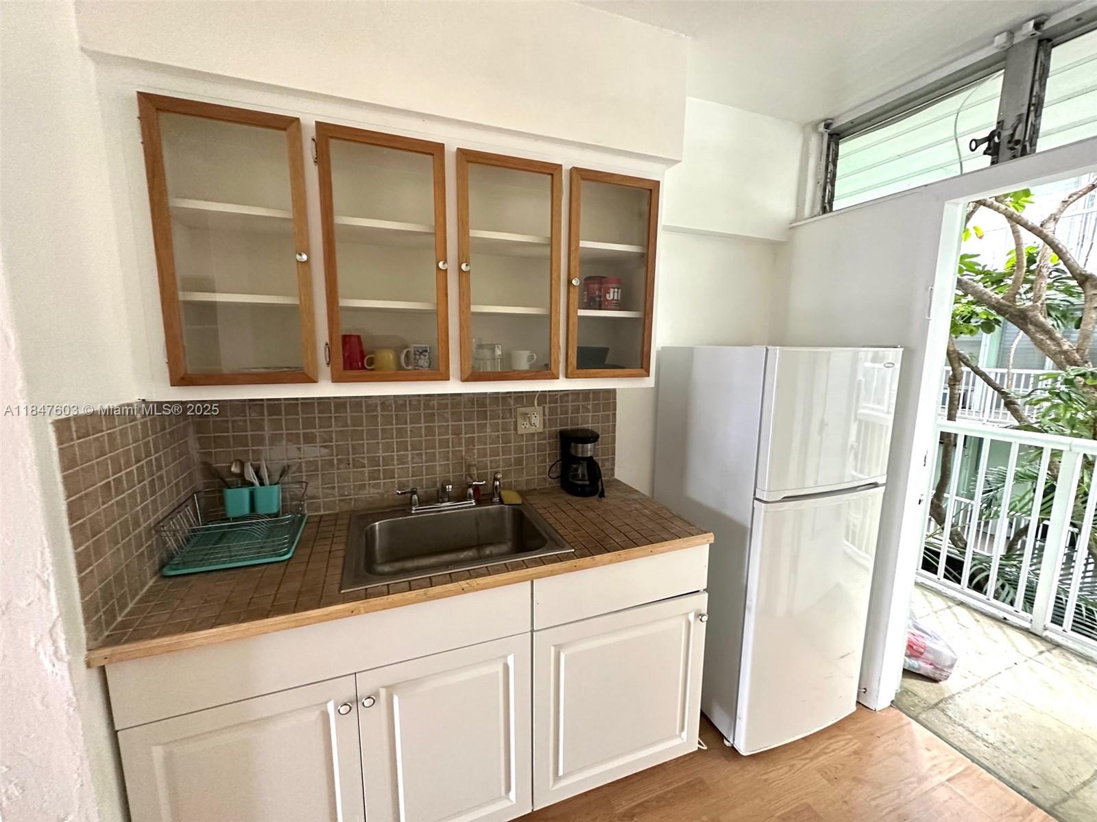 A kitchen features white cabinets, a tiled backsplash, a stainless steel sink, and a refrigerator — 1400 Pennsylvania Ave # 33, Miami Beach FL 33139, MIAMI BEACH, FL