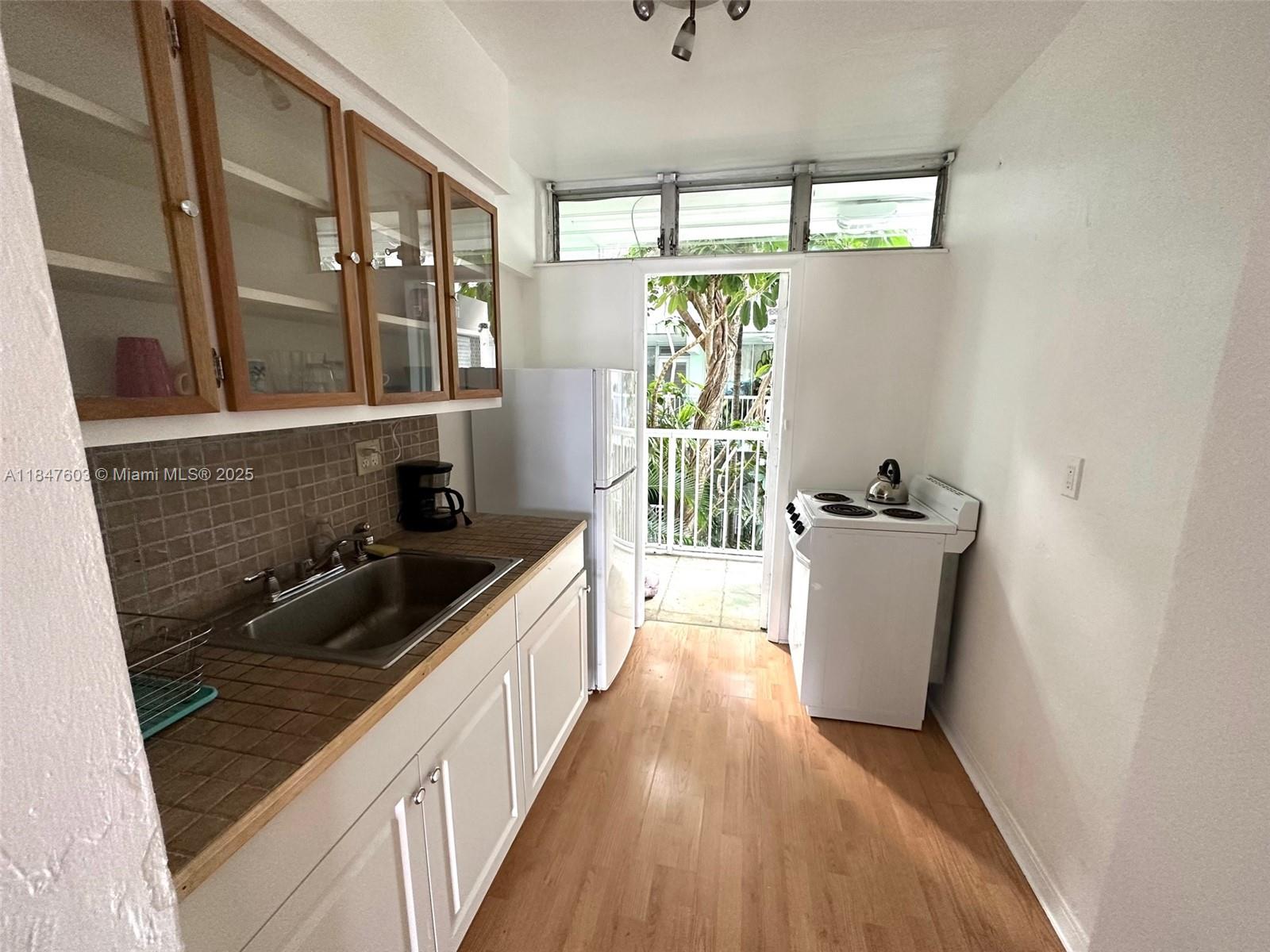 A galley kitchen features white cabinets, tiled countertops, a sink, appliances, and a balcony door — 1400 Pennsylvania Ave # 33, Miami Beach FL 33139, MIAMI BEACH, FL