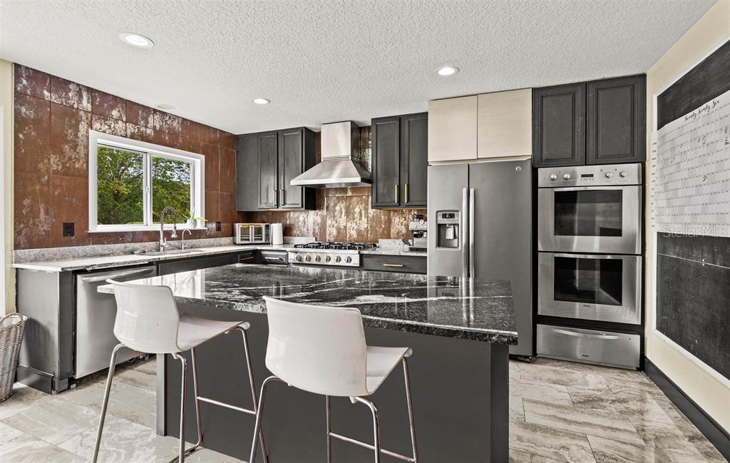 A kitchen features dark cabinets, a granite island with two chairs, and a metal backsplash — 5312 CYPRESS LINKS, ELKTON, FL