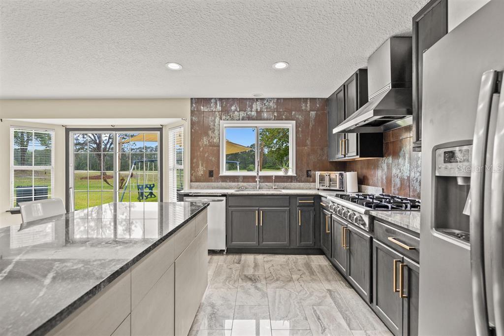 A kitchen features dark gray cabinetry, a granite island, and a metallic tile backsplash — 5312 CYPRESS LINKS, ELKTON, FL