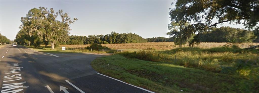 A paved road intersects with a large, grassy field bordered by trees under a clear sky — TBD HIGHWAY 441, ALACHUA, FL
