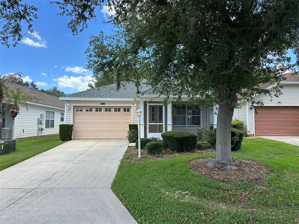 A single-story house with a beige garage, a front porch, and a concrete driveway — 25335 CRANES ROOST CIRCLE, LEESBURG, FL