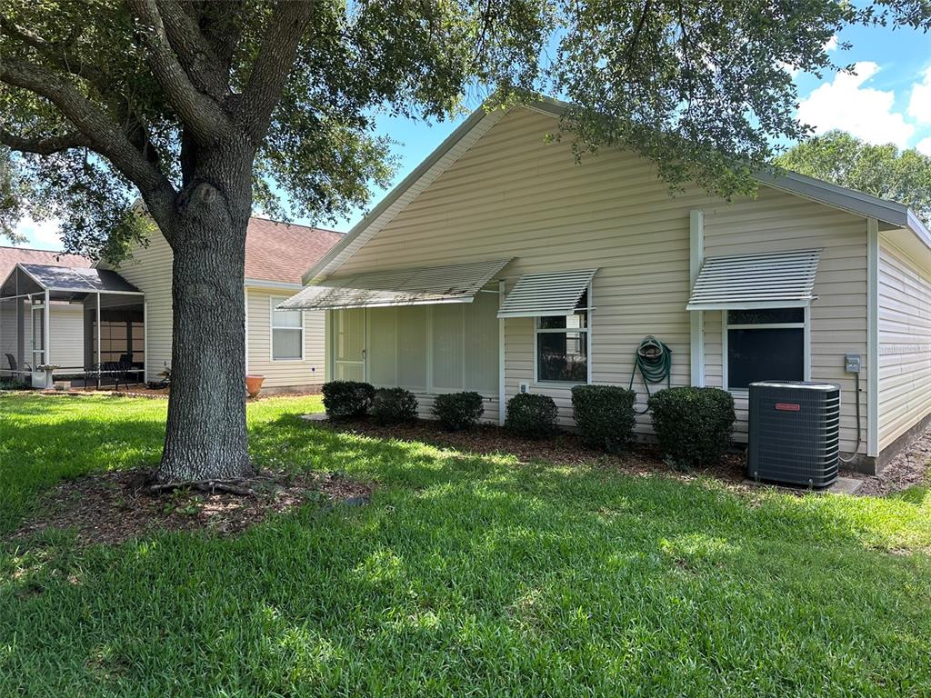 A side view of a beige vinyl-sided house with metal awnings and an air conditioning unit — 25335 CRANES ROOST CIRCLE, LEESBURG, FL