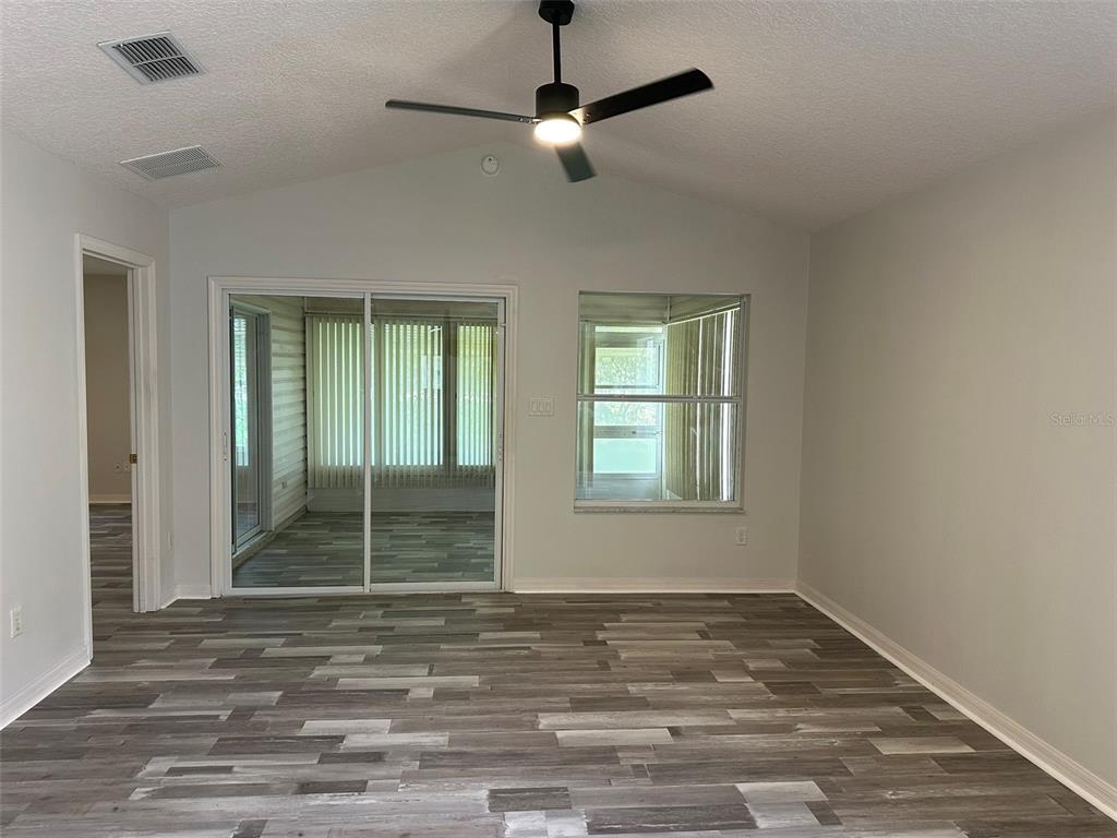 A living room with vaulted ceilings, gray wood-look flooring, a ceiling fan, and sliding doors — 25335 CRANES ROOST CIRCLE, LEESBURG, FL