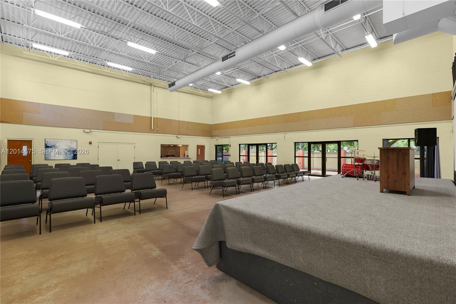 A large, open room features a stage, rows of chairs, and exposed industrial ceiling lighting — 8530 Stirling Rd, Davie FL 33024, DAVIE, FL