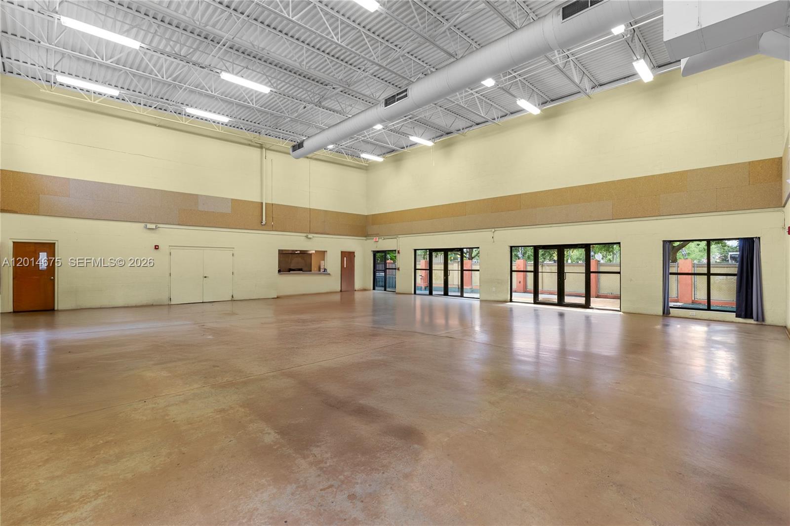 A large, open-concept room features high ceilings, concrete floors, and multiple glass-paneled doors — 8530 Stirling Rd, Davie FL 33024, DAVIE, FL