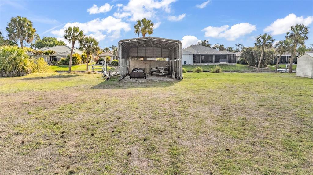 A metal carport sits in the middle of a grassy backyard with palm trees — 2410 /2418 COMO STREET, PORT CHARLOTTE, FL