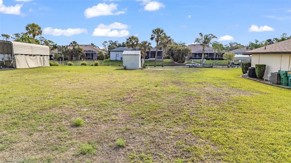 A large, grassy backyard features a small shed, a metal carport, and a canal view — 2410 /2418 COMO STREET, PORT CHARLOTTE, FL