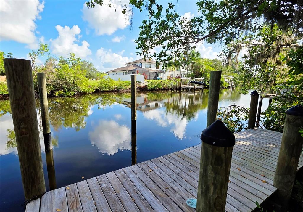 A wooden dock overlooks a calm canal with a house visible in the background — 3017 PINE STREET, BRADENTON, FL