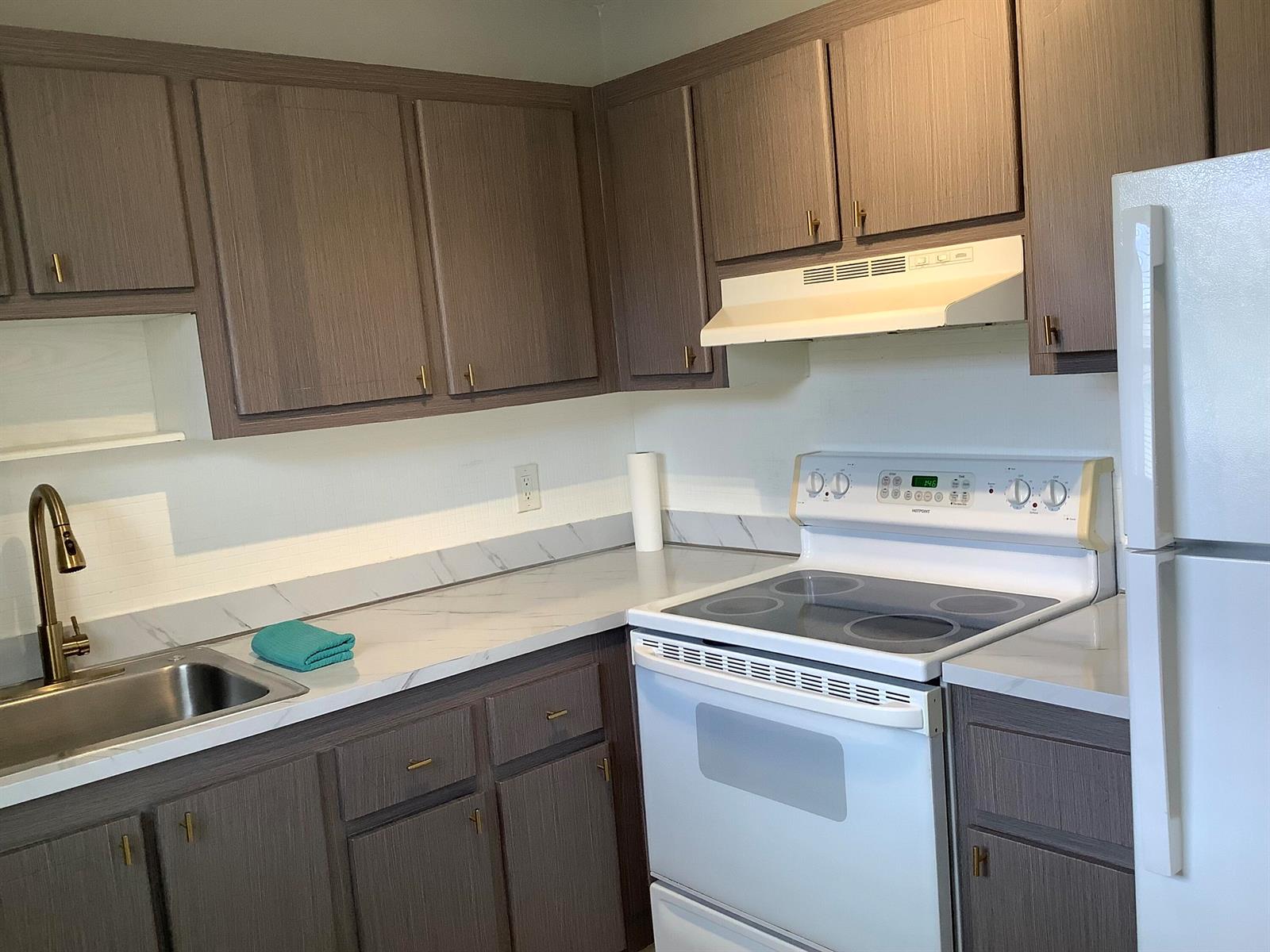 A kitchen features wood-grain cabinets, white appliances, and a marble-patterned countertop with a sink — 189 Saxony # 189, Delray Beach FL 33446, DELRAY BEACH, FL