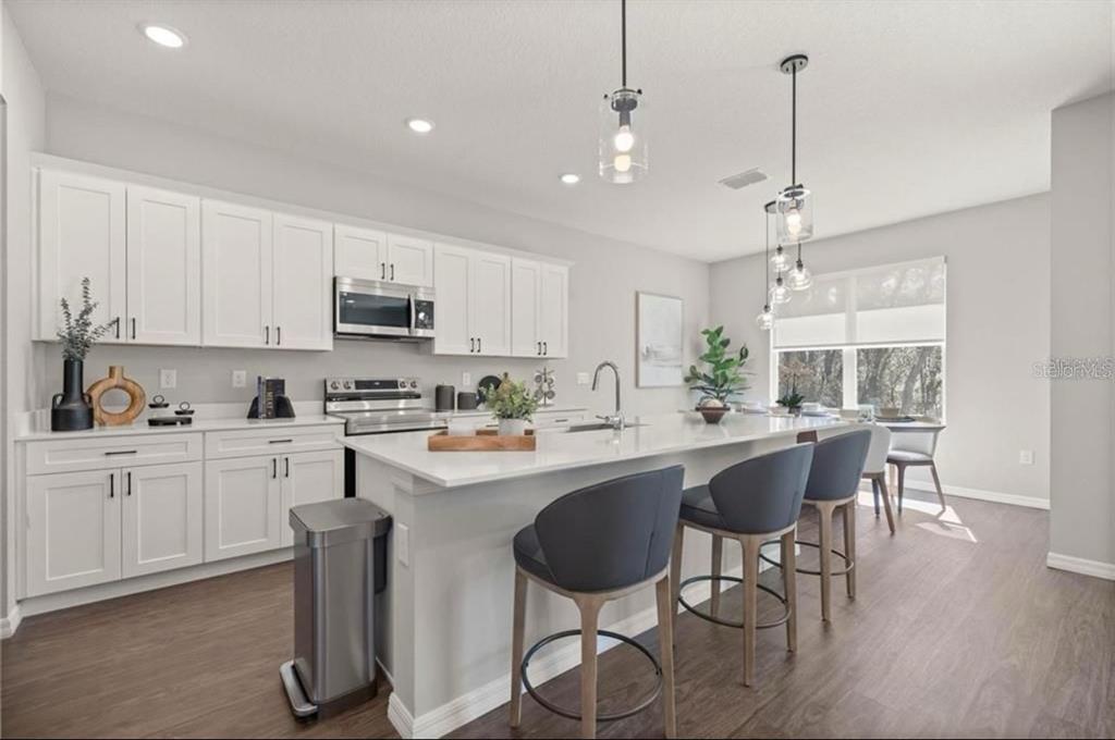 A modern kitchen features white cabinetry, a large island with bar seating, and stainless appliances — 8759 SW 138TH STREET, OCALA, FL