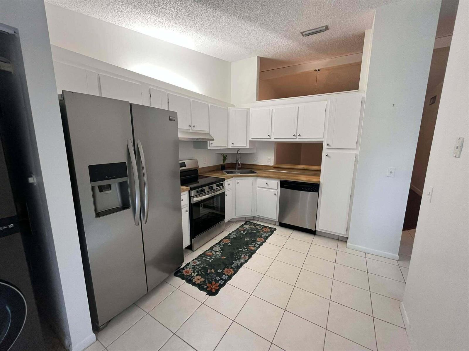A kitchen features white cabinets, stainless steel appliances, wood countertops, and light-colored tile flooring — 4863 Sable Pine Circle # D, West Palm Beach FL 33417, WEST PALM BEACH, FL