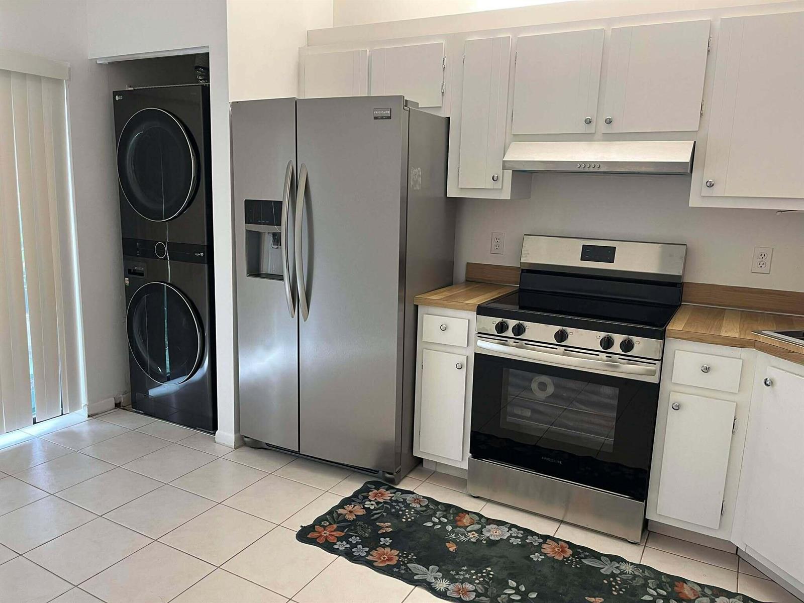 A kitchen features white cabinets, stainless steel appliances, a wood countertop, and a stacked washer-dryer — 4863 Sable Pine Circle # D, West Palm Beach FL 33417, WEST PALM BEACH, FL