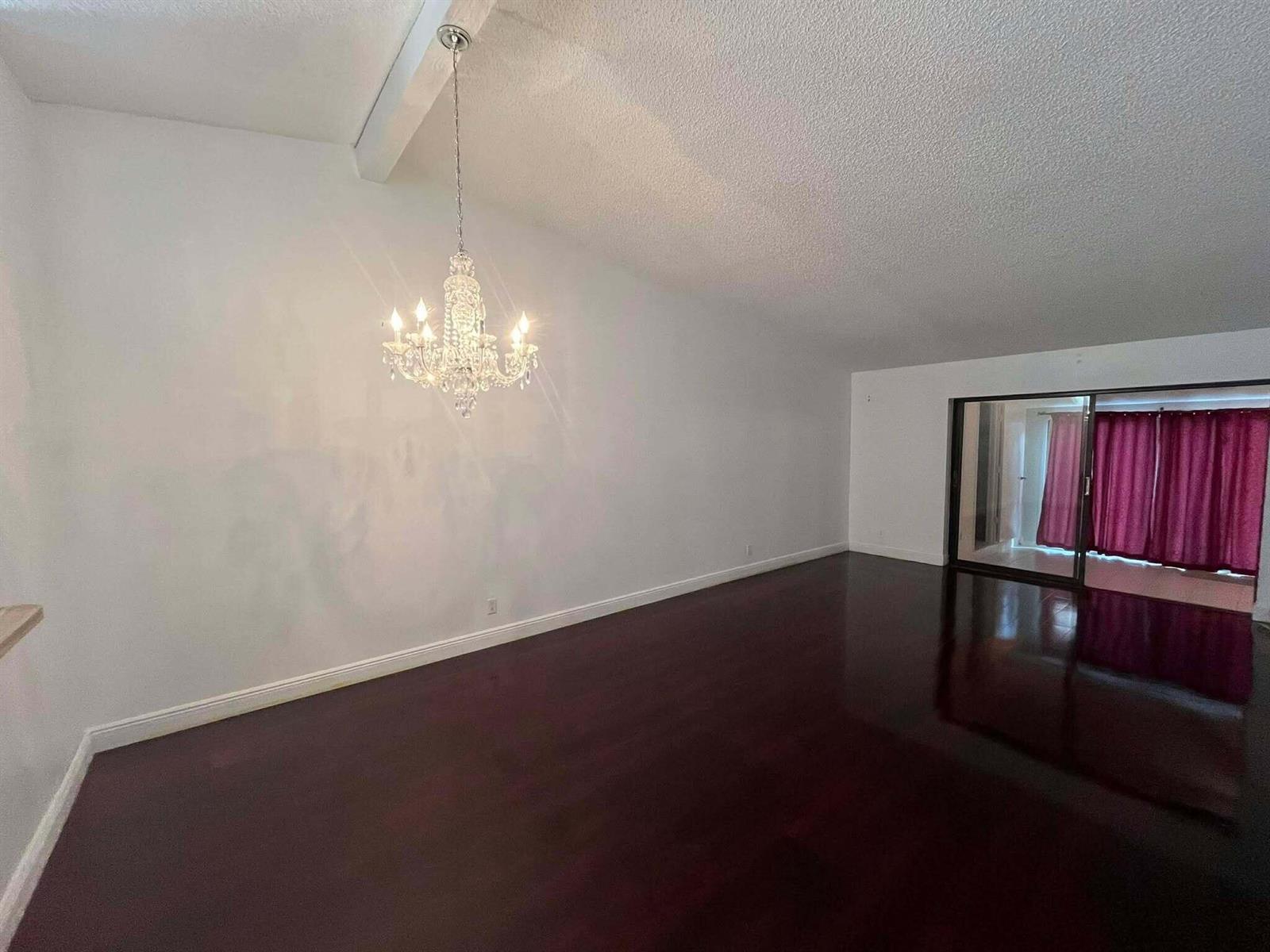 An empty room with dark hardwood floors, white walls, and a crystal chandelier — 4863 Sable Pine Circle # D, West Palm Beach FL 33417, WEST PALM BEACH, FL