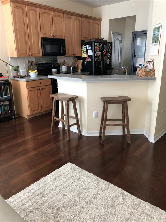 A kitchen features light wood cabinets, dark hardwood floors, and a breakfast bar with stools — 12982 KEGAN STREET, WINDERMERE, FL