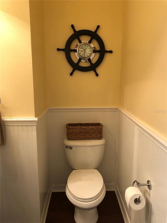 A bathroom features a white toilet, a wicker basket, and a nautical-themed ship wheel clock — 12982 KEGAN STREET, WINDERMERE, FL
