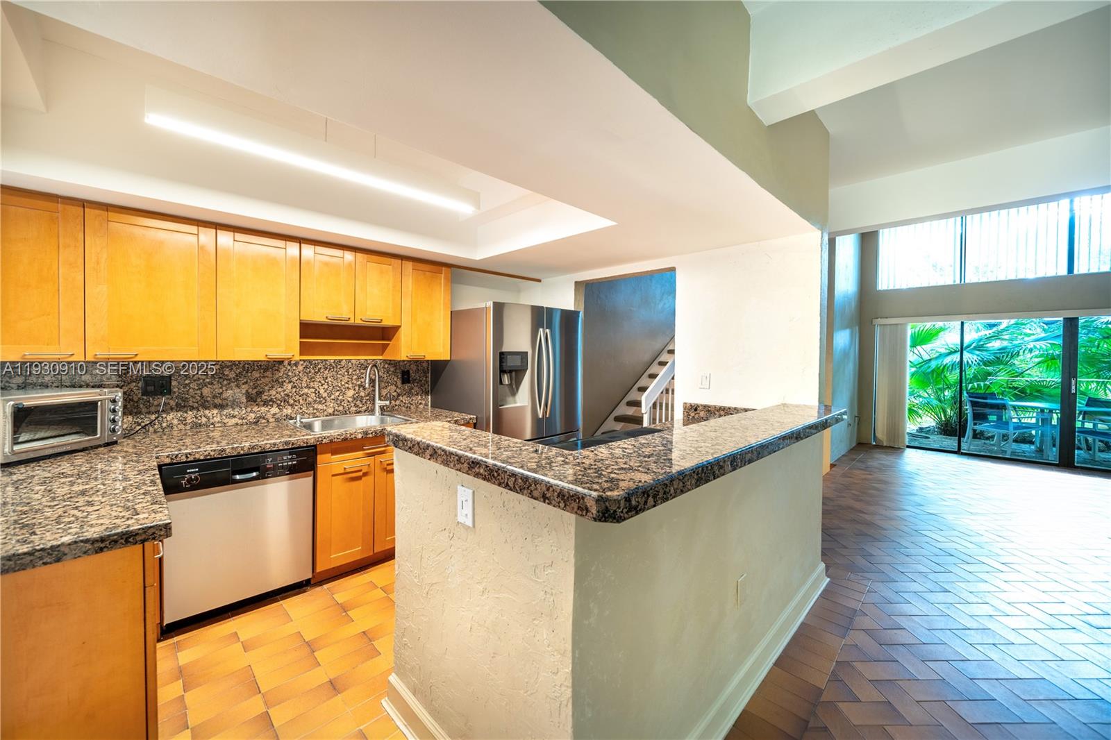 A kitchen with wood cabinets, granite countertops, and a breakfast bar overlooks a living area — 19212 NE 25th Ave # 283D, Miami FL 33180, MIAMI, FL
