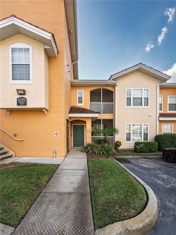 The exterior of a two-story tan stucco apartment building features a green front door — 12203 WILD IRIS WAY UNIT 108, ORLANDO, FL