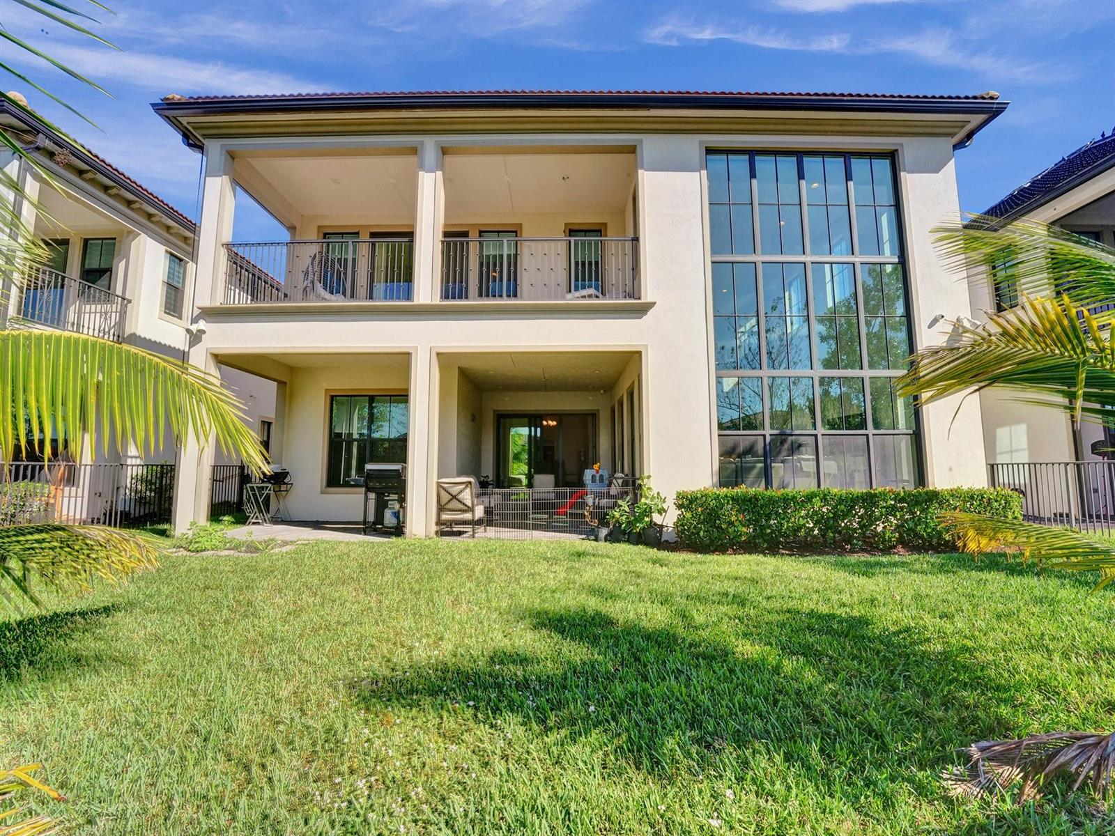 The rear exterior of a two-story house features a covered balcony, patio, and large windows — 9345 Carrington Avenue, Parkland FL 33076, PARKLAND, FL