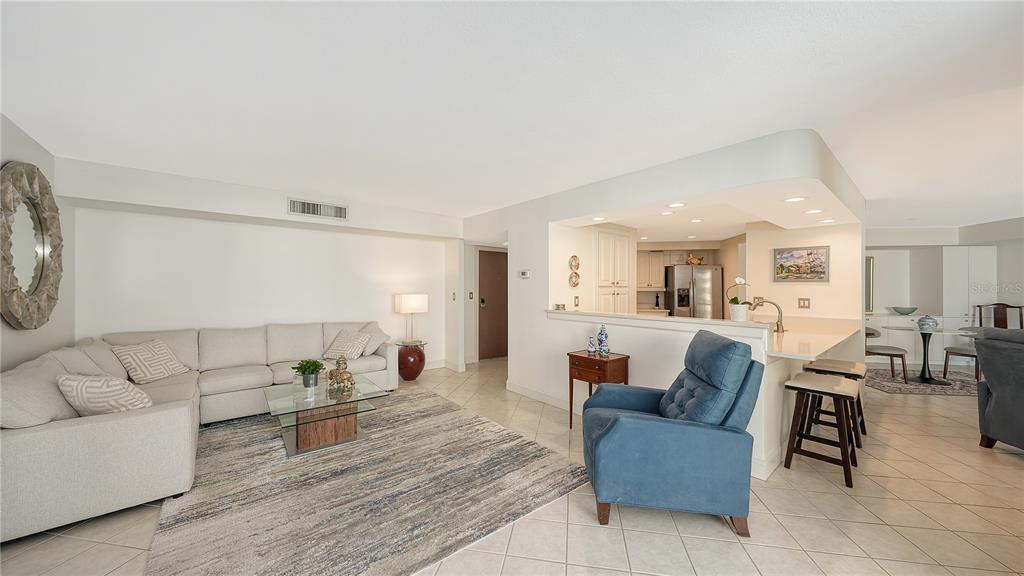 A living room features a sectional sofa, a blue armchair, and a balcony with views — 1111 N GULFSTREAM AVENUE UNIT 10E, SARASOTA, FL