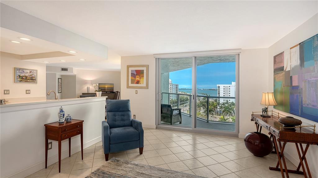 A living room features a blue armchair, a wooden console table, and sliding glass balcony doors — 1111 N GULFSTREAM AVENUE UNIT 10E, SARASOTA, FL