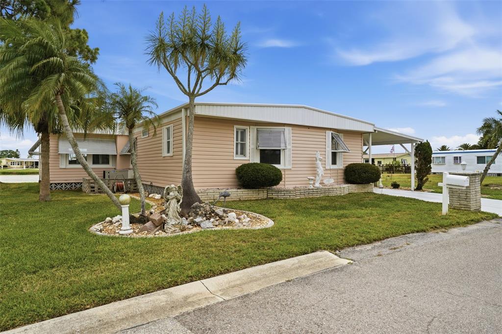 A light-colored mobile home with a carport, landscaping, and a lawn under a blue sky — 520 IMPERIAL DRIVE, NORTH PORT, FL
