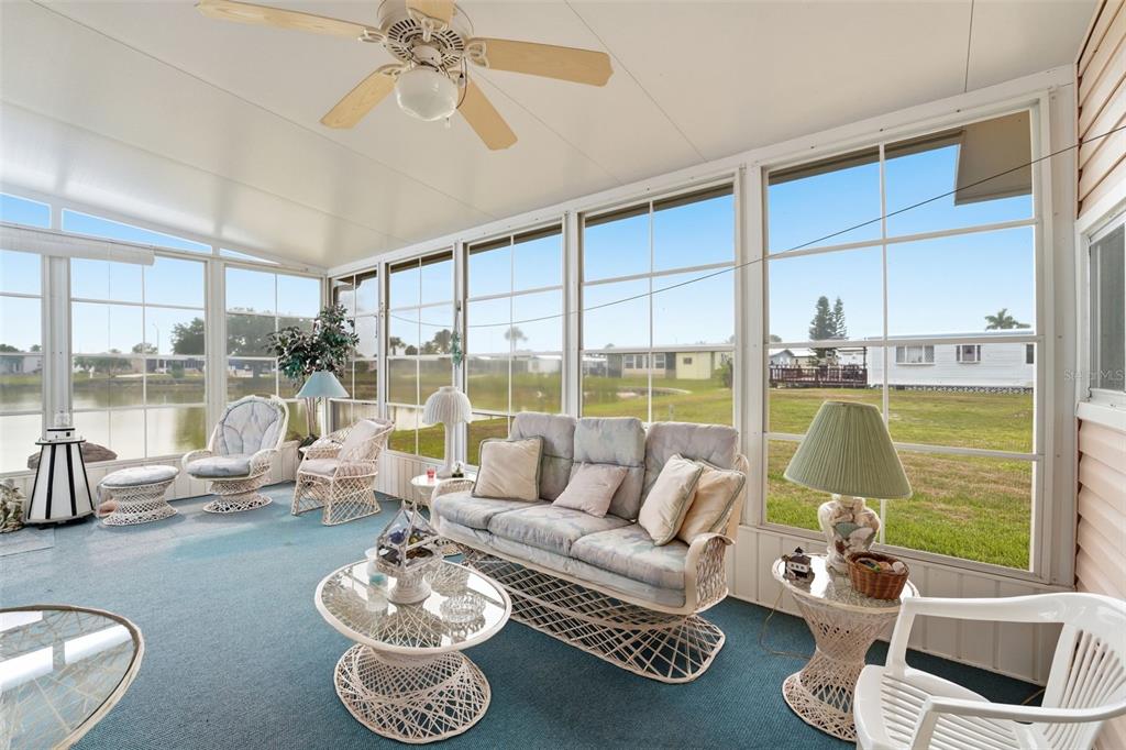 A sunroom with blue carpeting, wicker furniture, and large windows overlooking a pond and yard — 520 IMPERIAL DRIVE, NORTH PORT, FL