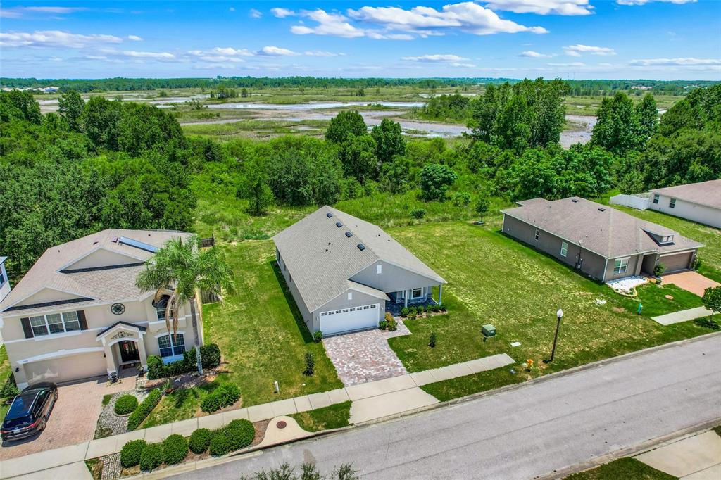 An aerial view shows three suburban houses with green lawns facing a marshy landscape — 3050 SUNSCAPE TERRACE, GROVELAND, FL