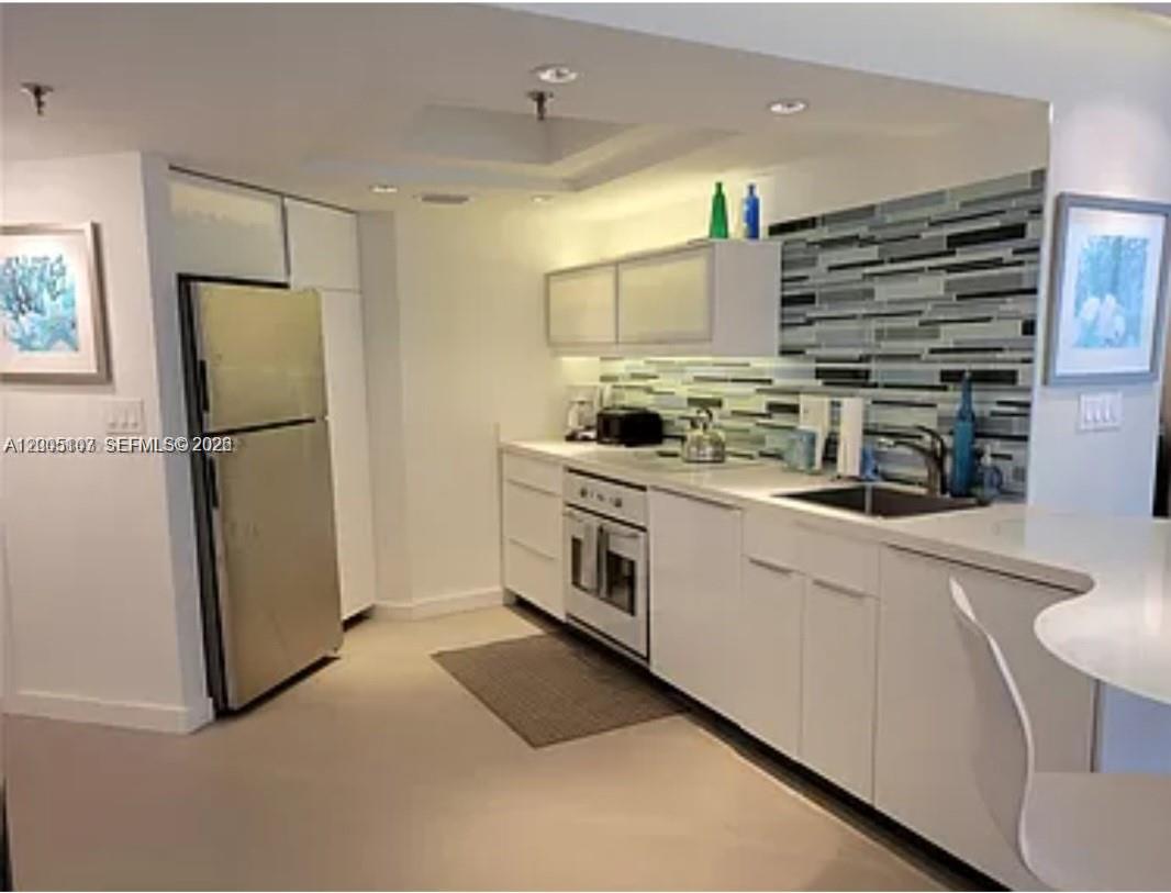 A modern kitchen features white cabinetry, stainless steel appliances, and a glass tile backsplash — 5880 Collins Ave # 604, Miami Beach FL 33140, MIAMI BEACH, FL