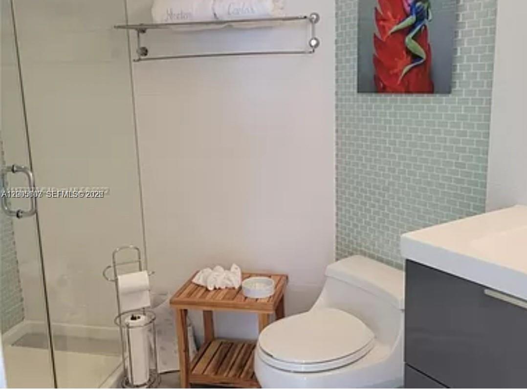 A bathroom features a glass-enclosed shower, a toilet, a wooden side table, and tiled walls — 5880 Collins Ave # 604, Miami Beach FL 33140, MIAMI BEACH, FL