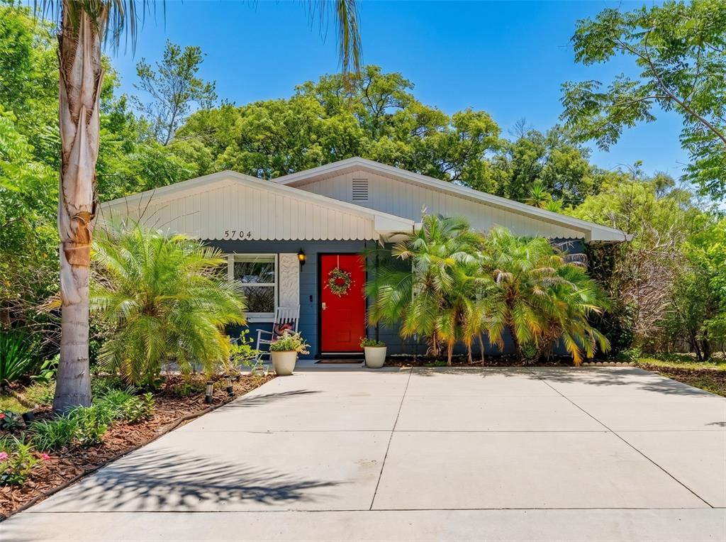 A blue house exterior features a red front door, a porch with two rocking chairs — 5704 13TH STREET, ZEPHYRHILLS, FL