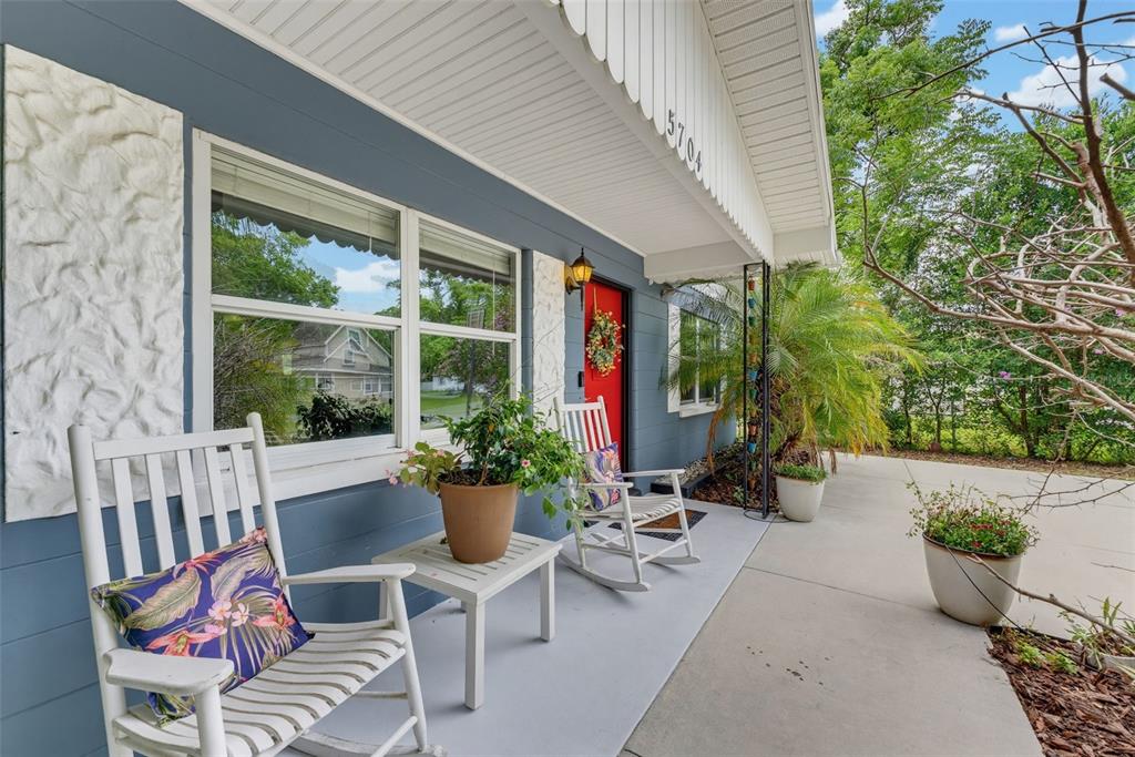 A blue house exterior features a bright red front door, white rocking chairs, and landscaping — 5704 13TH STREET, ZEPHYRHILLS, FL