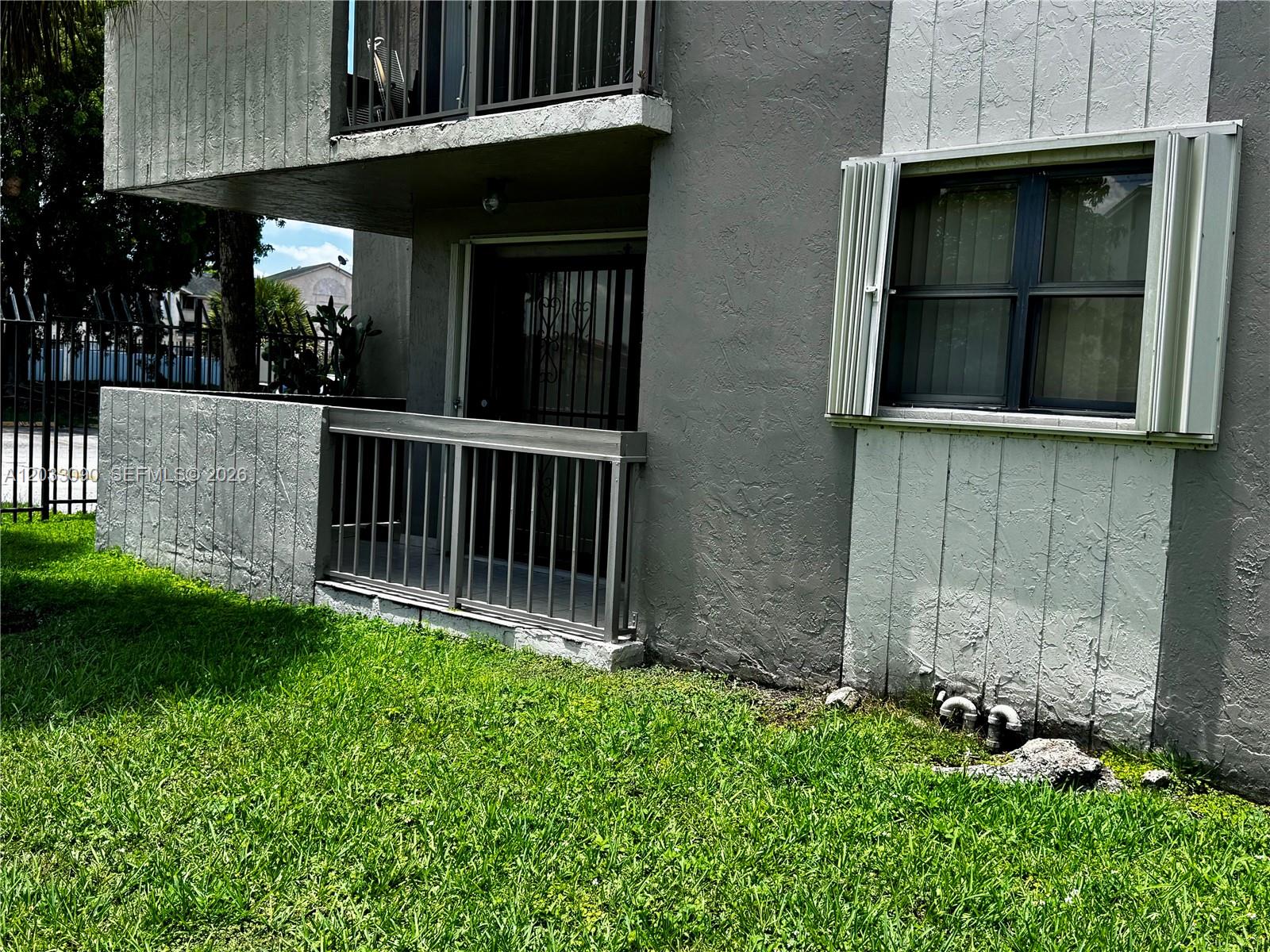 A ground-floor apartment exterior features a small patio with a metal railing and window shutters — 1121 SW 122nd Ave # 2, Miami FL 33184, MIAMI, FL