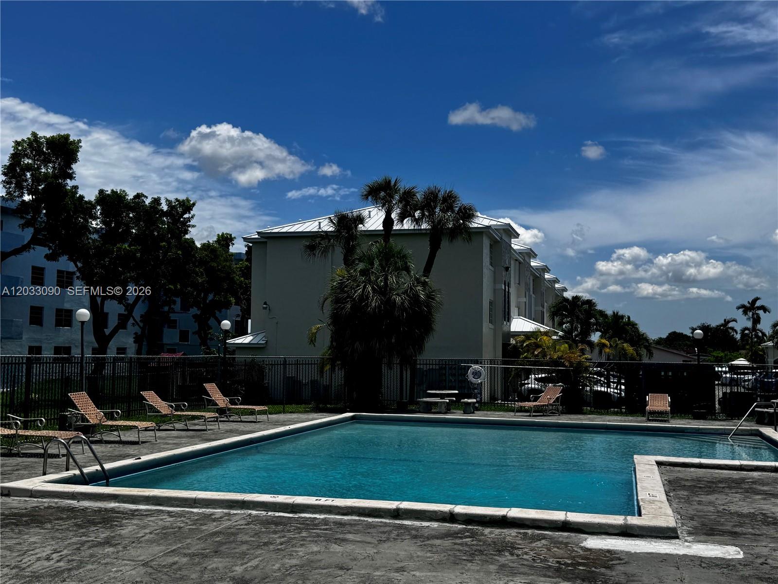 A swimming pool with lounge chairs sits in front of a multi-story apartment building — 1121 SW 122nd Ave # 2, Miami FL 33184, MIAMI, FL