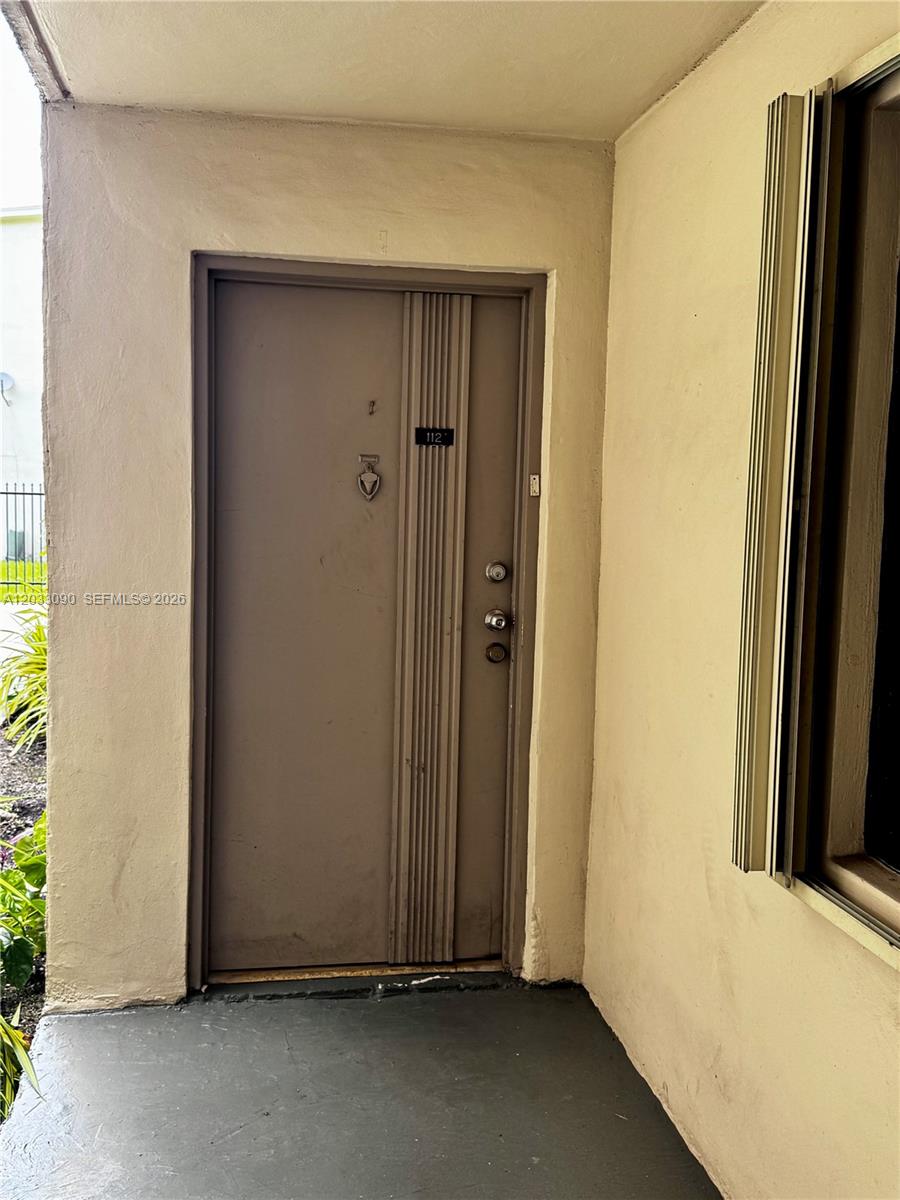 A beige front door with a silver knocker and handle is set in a stucco wall — 1121 SW 122nd Ave # 2, Miami FL 33184, MIAMI, FL