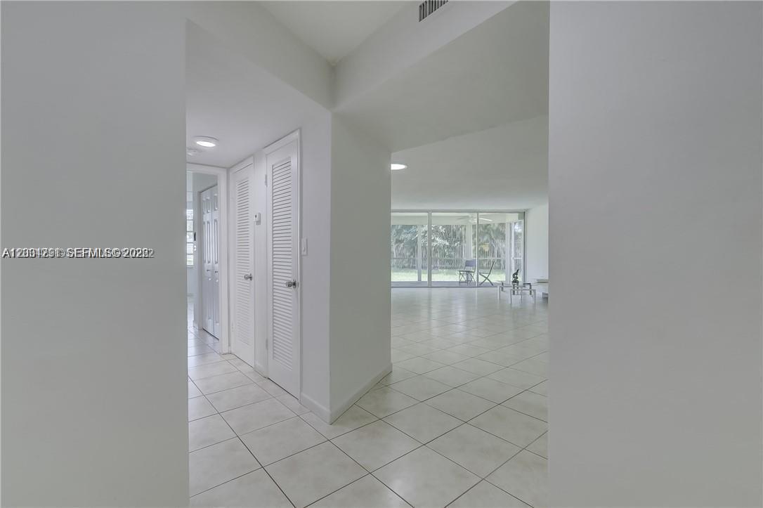 A white-walled hallway with tiled floors leads to an open living area with large windows — 1351 NE 191st St # E117, Miami FL 33179, MIAMI, FL