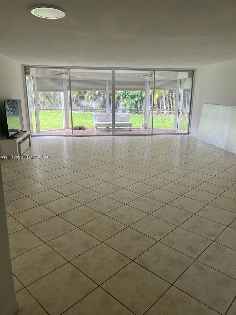 A spacious living room features light-colored tile flooring, large sliding glass doors, and a patio — 1351 NE 191st St # E117, Miami FL 33179, MIAMI, FL