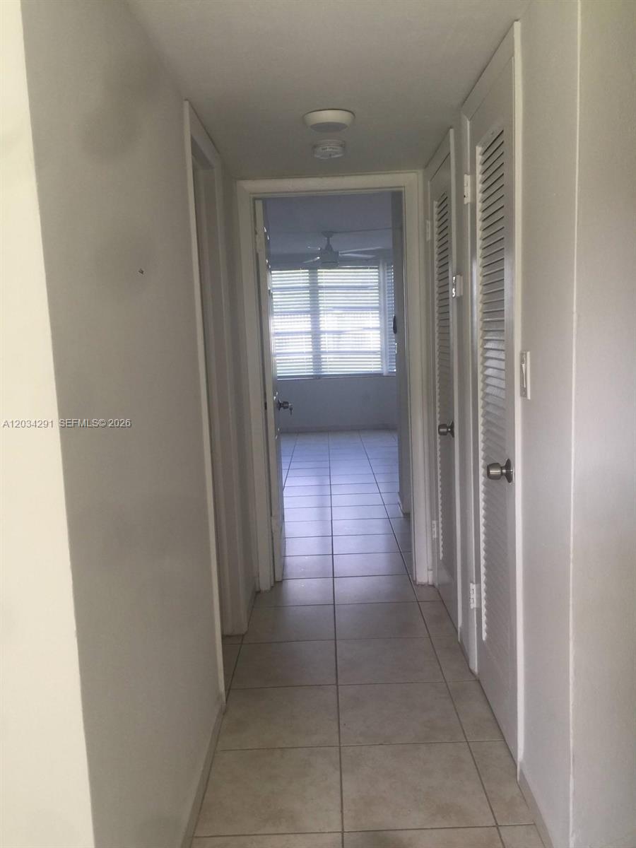 A hallway with tiled floors leads to a room with a window and ceiling fan — 1351 NE 191st St # E117, Miami FL 33179, MIAMI, FL