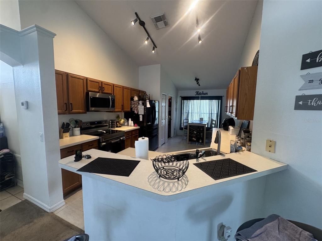 A kitchen features wood cabinets, a breakfast bar, and a dining area in the background — 4612 FALCON AVENUE, KISSIMMEE, FL