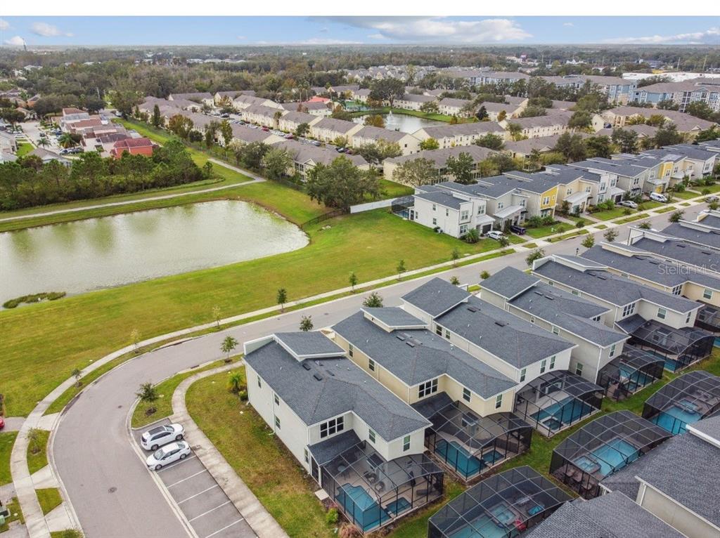 An aerial view shows a row of townhomes with screened-in pools beside a retention pond — 2784 BOOKMARK DRIVE, KISSIMMEE, FL