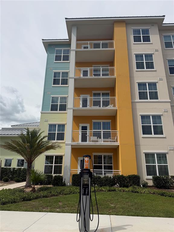 A multi-story apartment building features colorful exterior siding, balconies, and an electric vehicle charging station — 3151 SUNSET WALK DRIVE UNIT 116, KISSIMMEE, FL