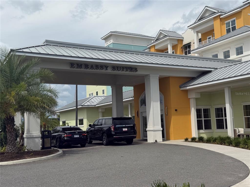 The exterior of an Embassy Suites hotel features a covered entrance with two parked cars — 3151 SUNSET WALK DRIVE UNIT 116, KISSIMMEE, FL