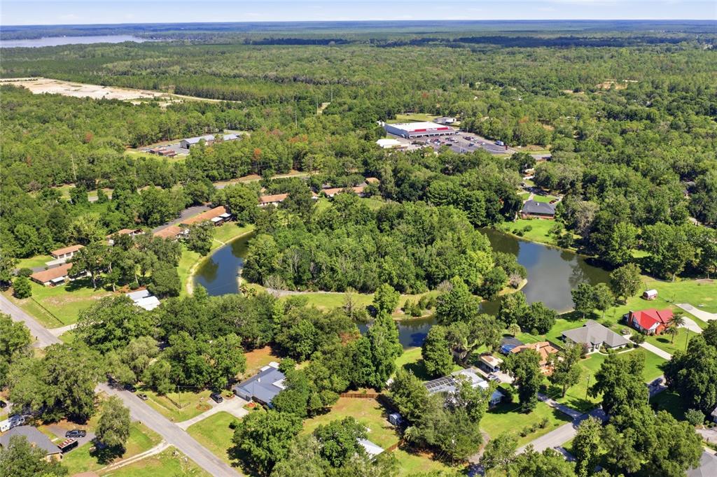 An aerial view shows a residential neighborhood surrounding a curved pond amidst dense trees — 561 SE 28TH STREET, MELROSE, FL