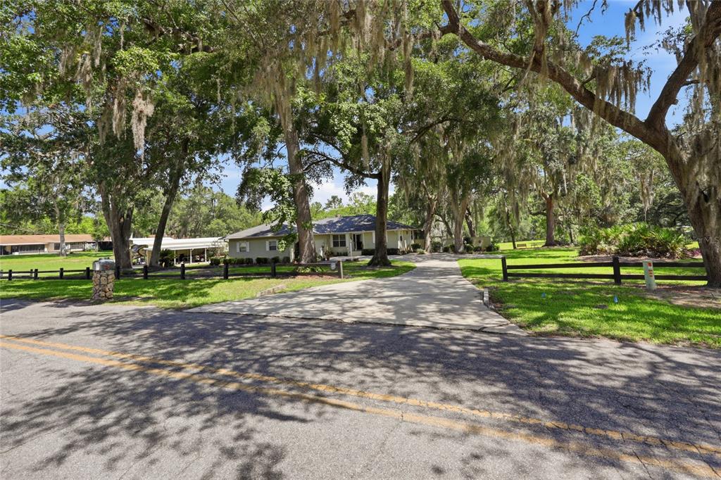 A single-story house with a concrete driveway sits behind a wooden fence under large trees — 561 SE 28TH STREET, MELROSE, FL