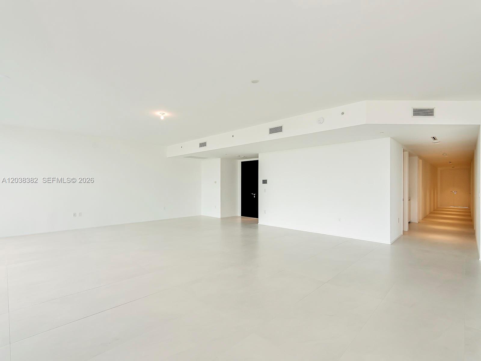 An empty, minimalist room features white walls, light-colored tile flooring, and a long hallway — 1000 Biscayne Blvd # 2002, Miami FL 33132, MIAMI, FL