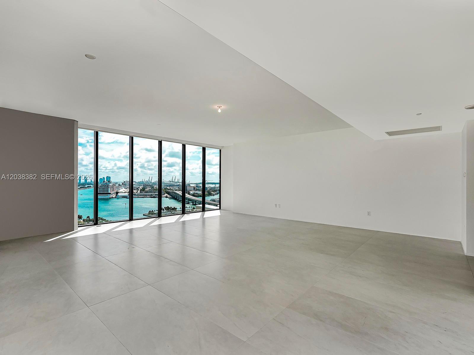 An empty room with large floor-to-ceiling windows overlooking a harbor and city skyline — 1000 Biscayne Blvd # 2002, Miami FL 33132, MIAMI, FL